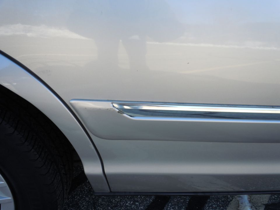 Silver sedan with damaged chrome trim and rear tire.
