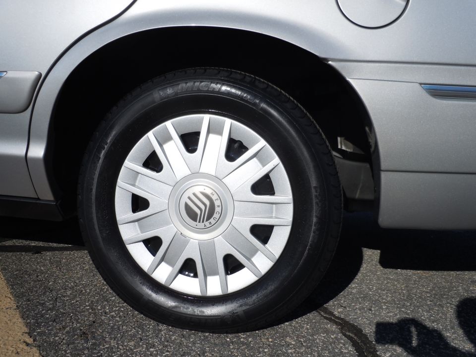 Silver sedan rear wheel and fender with Michelin tire and Mercury logo hubcap.