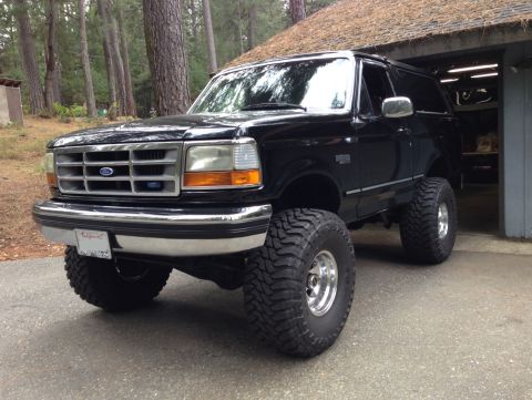 1993 Ford Bronco - A lifted black 1993 Ford Bronco with large off-road tires is parked in front of a garage. The vehicle has a chrome grille and bumper, and a…