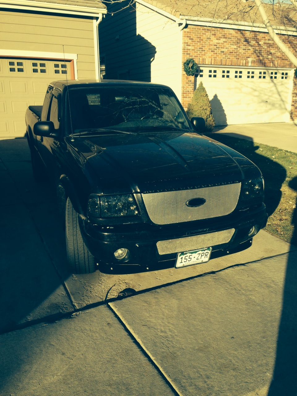 Black Ford Ranger pickup truck with custom grille and cracked windshield parked in driveway.