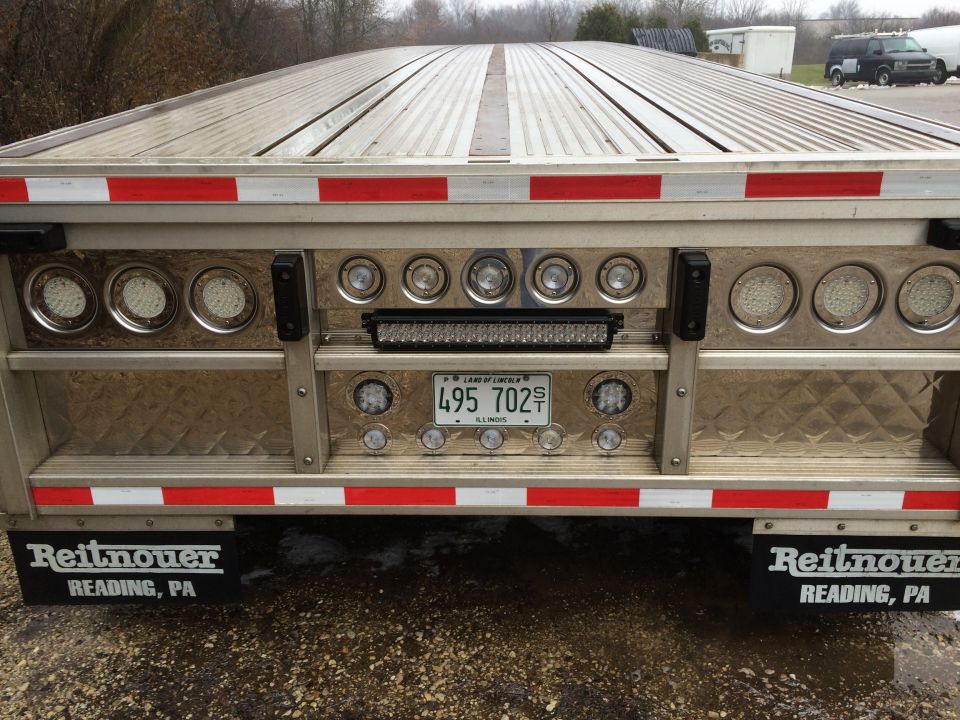 Rear of a flatbed trailer with LED lights, license plate, and Reitnauer branding.