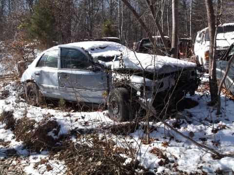 1974 Dodge Challenger - A damaged, light blue sedan sits in a snowy wooded area, partially obscured by branches. The front end of the vehicle is heavily damaged an…