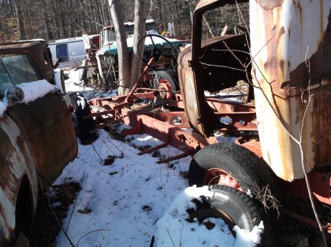1974 Dodge Challenger - A rusty, disassembled vehicle chassis sits in the snow, surrounded by trees. Parts of other vehicles, including tires and a trailer, are vi…