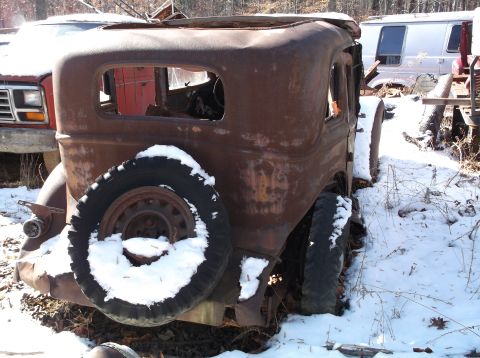 1974 Dodge Challenger - A heavily rusted vintage car with a spare tire mounted on the rear is parked in a snowy, wooded area. A red truck is visible to the left, a…