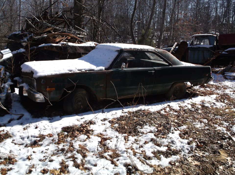 Dark green sedan covered in snow in a junkyard.