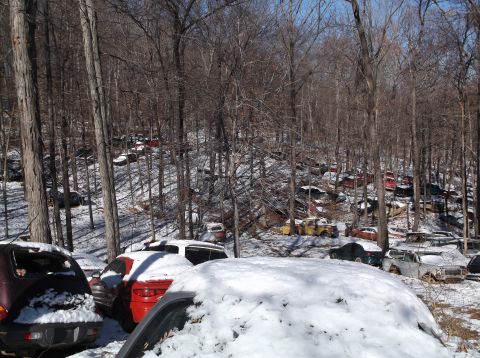 1974 Dodge Challenger - A junkyard scene with numerous old cars and trucks covered in snow, nestled amongst bare trees on a hillside.