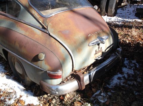 1974 Dodge Challenger - The rear passenger side of a heavily rusted, vintage Plymouth coupe is shown parked outdoors in a wooded area with patches of snow on the g…