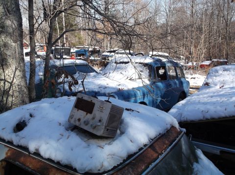 1974 Dodge Challenger - Several old cars are parked in a snowy junkyard. A blue station wagon is prominent in the foreground, partially covered in snow, with a vin…