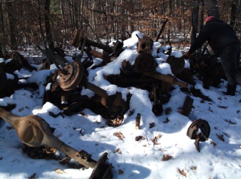 1974 Dodge Challenger - A pile of rusty, snow-covered vehicle axle assemblies and parts are scattered in a wooded area. A person in dark clothing and a pink hat is…