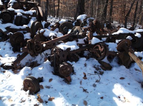 1974 Dodge Challenger - A pile of rusty, snow-covered vehicle axles and brake assemblies are scattered in a wooded area.