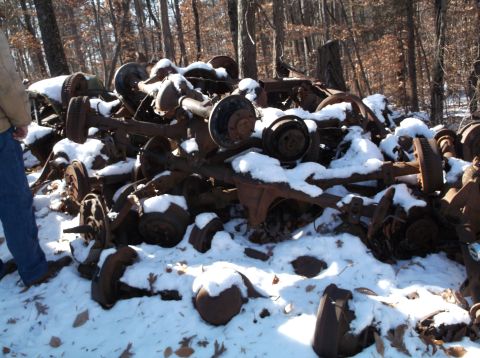 1974 Dodge Challenger - A pile of rusty, snow-covered vehicle axle assemblies and differential housings are piled in a wooded area. A person's legs and blue jeans…