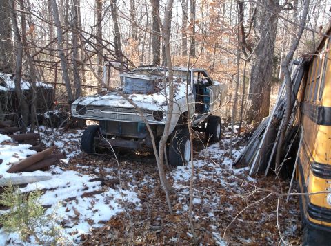 1974 Dodge Challenger - A heavily modified, lifted vehicle, possibly a muscle car, sits in a wooded area with snow on the ground. A yellow school bus is partially…