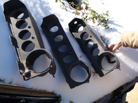 1974 Dodge Challenger - Three black plastic gauge cluster housings are laid out on a snowy surface. The housings have multiple circular cutouts for gauges and are…