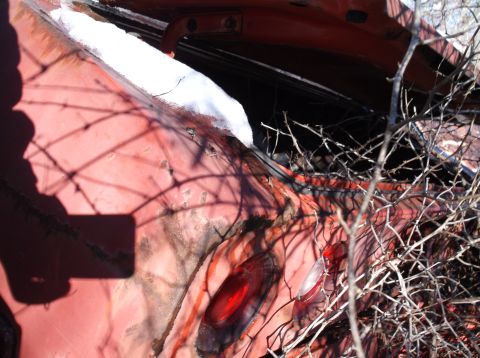1974 Dodge Challenger - A close-up view of the rear quarter panel of a red vintage car, likely a 1974 Dodge Challenger, with a broken taillight and snow on the tru…