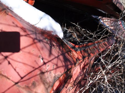 1974 Dodge Challenger - A close-up view of the weathered, red exterior of a vehicle, possibly a 1974 Dodge Challenger, with snow accumulated on the upper edge and…