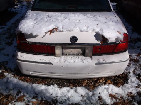1974 Dodge Challenger - The rear of a white Mercury Grand Marquis LSE is covered in snow and fallen leaves. The car is parked outdoors on a dirt and leaf-covered s…