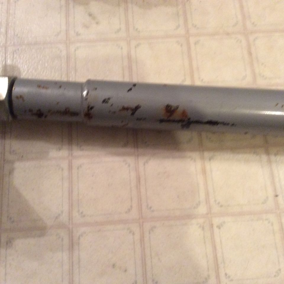 Gray metal pole with rust spots on a tiled floor.