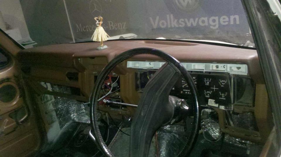 Interior of a car showing a brown dashboard, steering wheel, and exposed wiring.