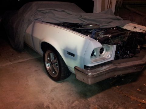 1976 Ford Ranchero - A partially covered classic car, likely a 1976 Ford Ranchero, is shown with its hood open, revealing the engine bay. The front end of the c…