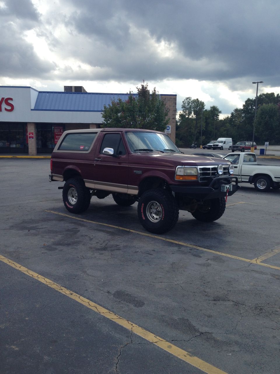 Maroon lifted Ford Bronco with off-road tires parked in front of a store.