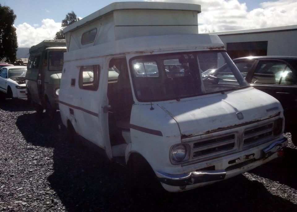 White camper van with open door, parked in a gravel lot.