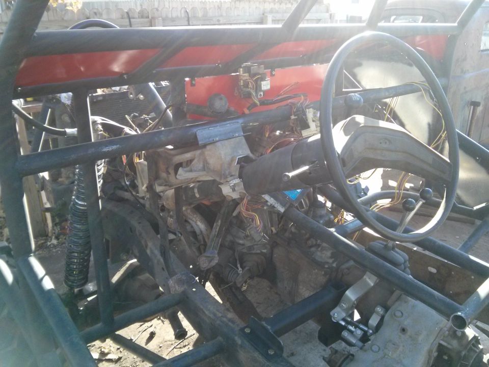 Interior of a custom buggy with steering wheel, exposed wiring, and roll cage.