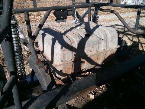 1986 Ford Bronco - A rusty, rectangular metal fuel tank is mounted within the frame of a custom off-road vehicle. The tank is surrounded by black metal tubing…