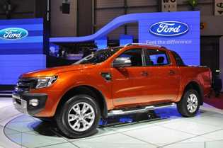 1982 Ford Bronco - A bright orange Ford Ranger pickup truck is displayed on a rotating platform in front of a Ford logo and blue lighting. The truck is shown…