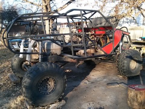1986 Ford Bronco - A custom-built off-road buggy with a roll cage and large tires is parked outdoors on a dirt and concrete surface.