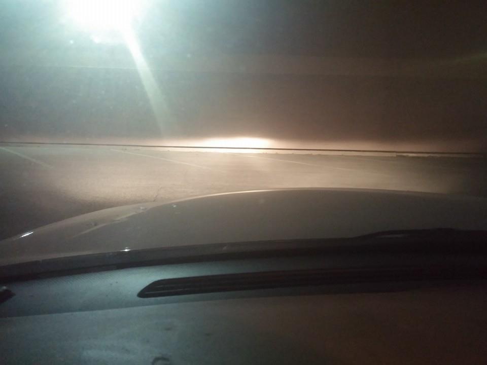 Photo of headlight beam on pavement seen over a car hood at night