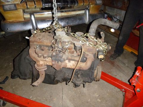 1953 Plymouth Belvedere - A rusty engine is being hoisted by chains, with the front end of a vintage car visible in the background.