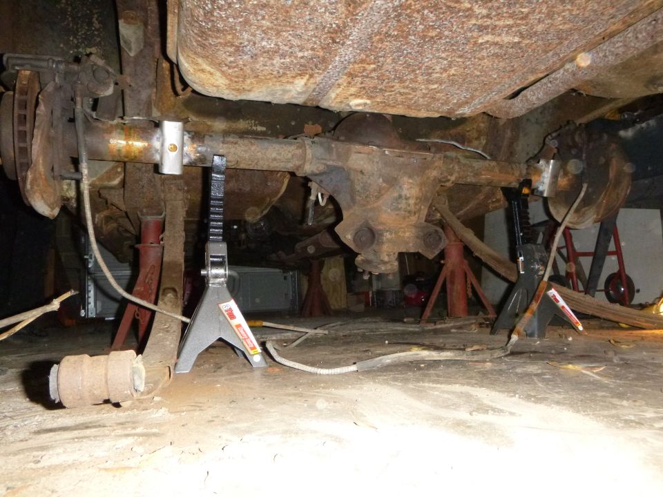 Rusty rear axle assembly supported by jack stands, with brake drums visible
