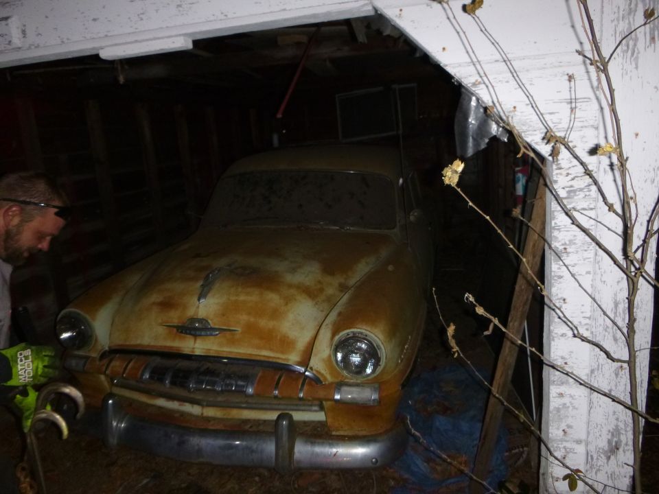 Old rusty sedan in a garage. Grille and headlights visible