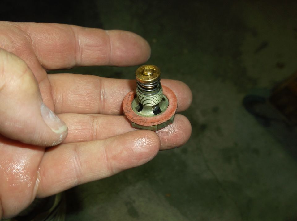 Hand holding a thermostat valve with a red gasket and spring