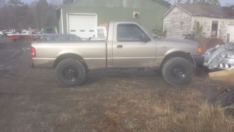 1991 Ford Bronco - A gold pickup truck is seen from the side, parked on a dirt lot with a building in the background.