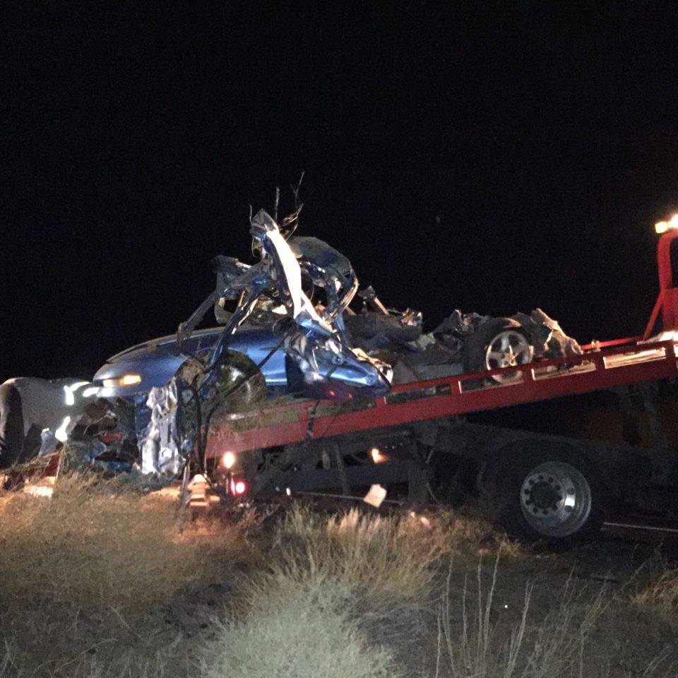 Wrecked blue car loaded onto a red tow truck at night