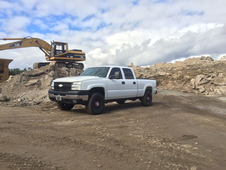White 2006 Chevrolet Silverado 2500 parked on dirt with an excavator behind it