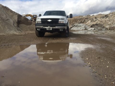 2006 Chevrolet Silverado 2500 - A white Chevrolet Silverado pickup truck is parked in a quarry, its reflection visible in a muddy puddle.