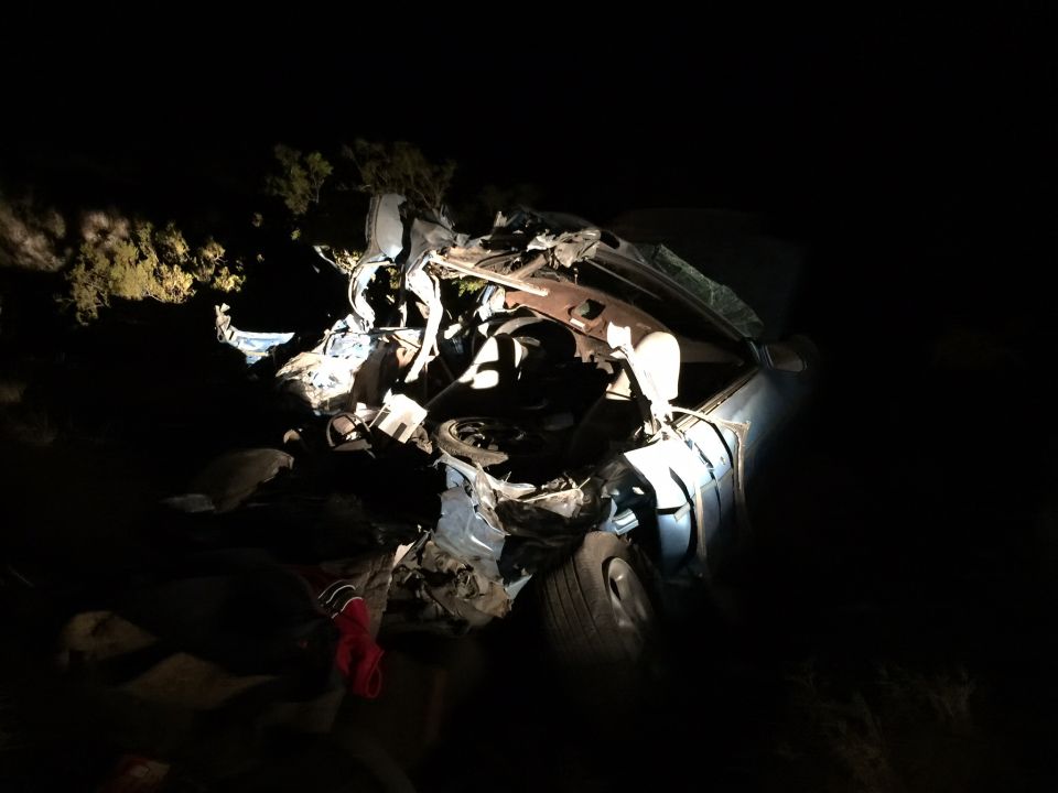 wrecked car at night, front end destroyed, engine exposed, tire visible