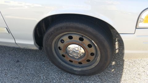 1991 Ford LTD Crown Victoria - Close-up of a silver car's front fender and wheel, a steel rim with a Ford hubcap and visible tire tread.