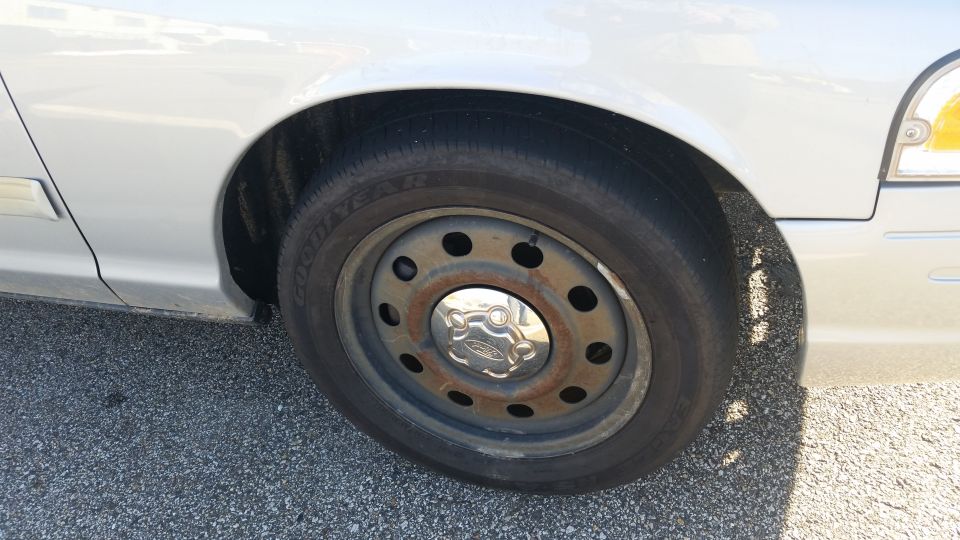 Silver car fender and wheel with a steel rim and Ford hubcap. Visible tire tread