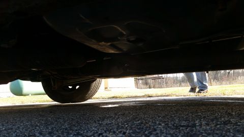1991 Ford LTD Crown Victoria - View of the underside of a car, including the exhaust system and a rear tire, with a person visible in the background.