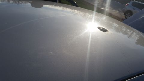 1991 Ford LTD Crown Victoria - The sun reflects off the hood of a car, highlighting a small dent and scratches. Another vehicle is parked nearby.