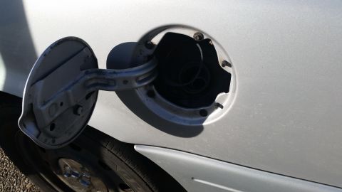 1991 Ford LTD Crown Victoria - Close-up of an open gas cap door on a silver vehicle, revealing the fuel filler neck and a portion of the tire.