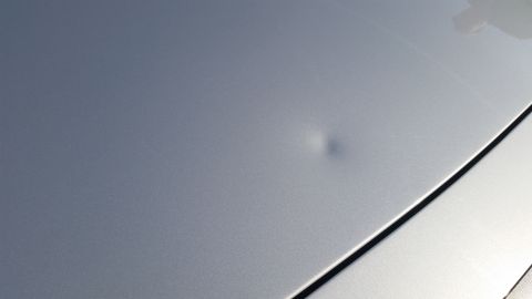 1991 Ford LTD Crown Victoria - A close-up shot of a silver car's hood shows a noticeable dent.
