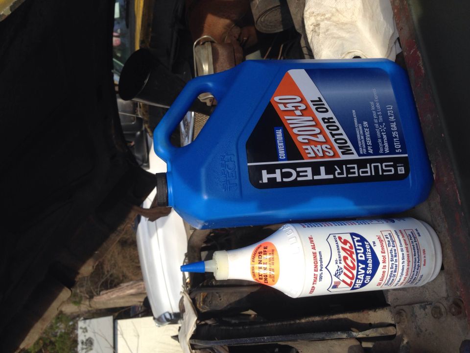Motor oil and oil stabilizer bottles on a dark surface, possibly in a vehicle engine bay