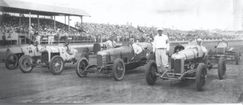 1909 Ford Model T - A group of vintage race cars are gathered on a track, possibly before an event.