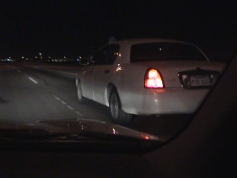 2002 Lincoln Town Car - A white sedan is seen from behind on a highway at night, with its taillights illuminated.