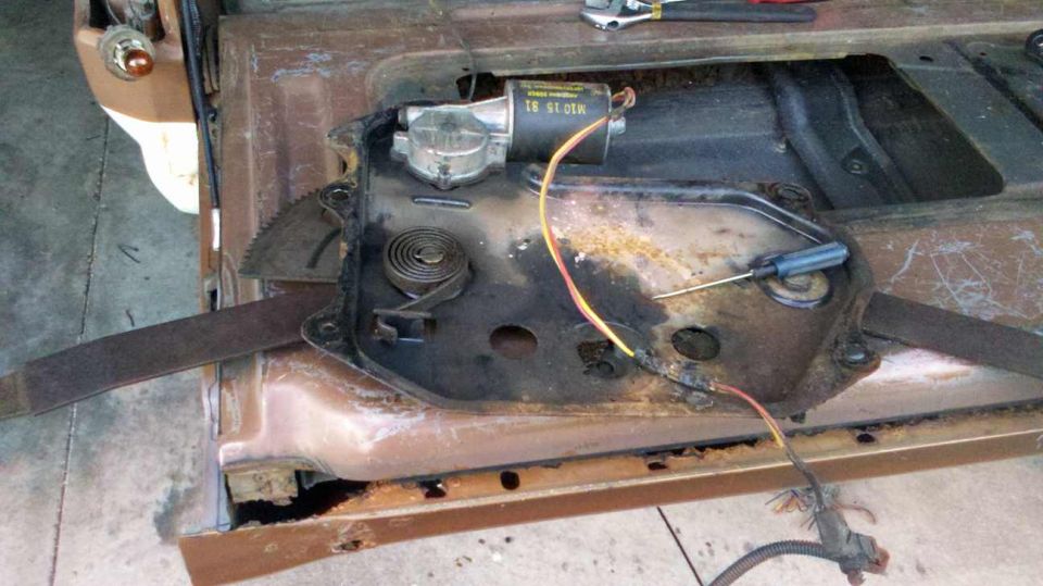 Rusty car door window regulator with motor and wires, screwdriver on mechanism