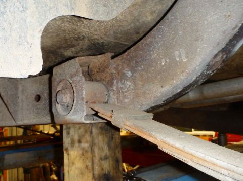 1964 Mercury Monterey - Close-up view of a rusty leaf spring suspension component, supported by wood, with a watermark at the bottom.